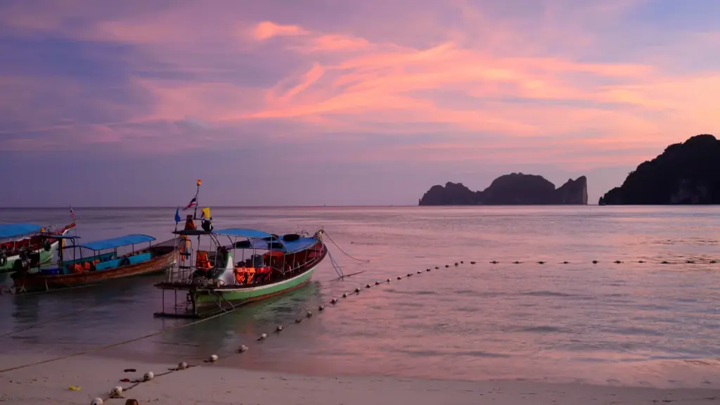 Longtail boats beside a Thai island beach at sunset